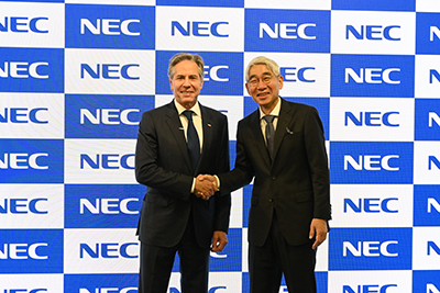 US Foreign Secretary Blinken poses for a photo with NEC President and CEO Takayuki Morita in front of a wall of blue and white NEC logos to promote Open RAN